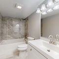 Modern white bathroom with tub, toilet, vanity sink, large mirror, and tiled shower wall