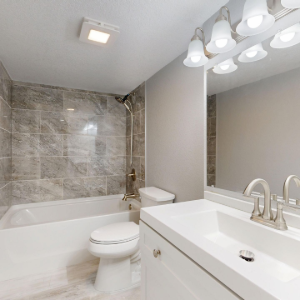 Modern white bathroom with tub, toilet, vanity sink, large mirror, and tiled shower wall