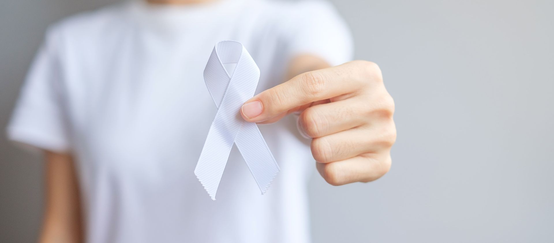 Mão segurando um laço branco, símbolo de conscientização sobre o câncer de pulmão