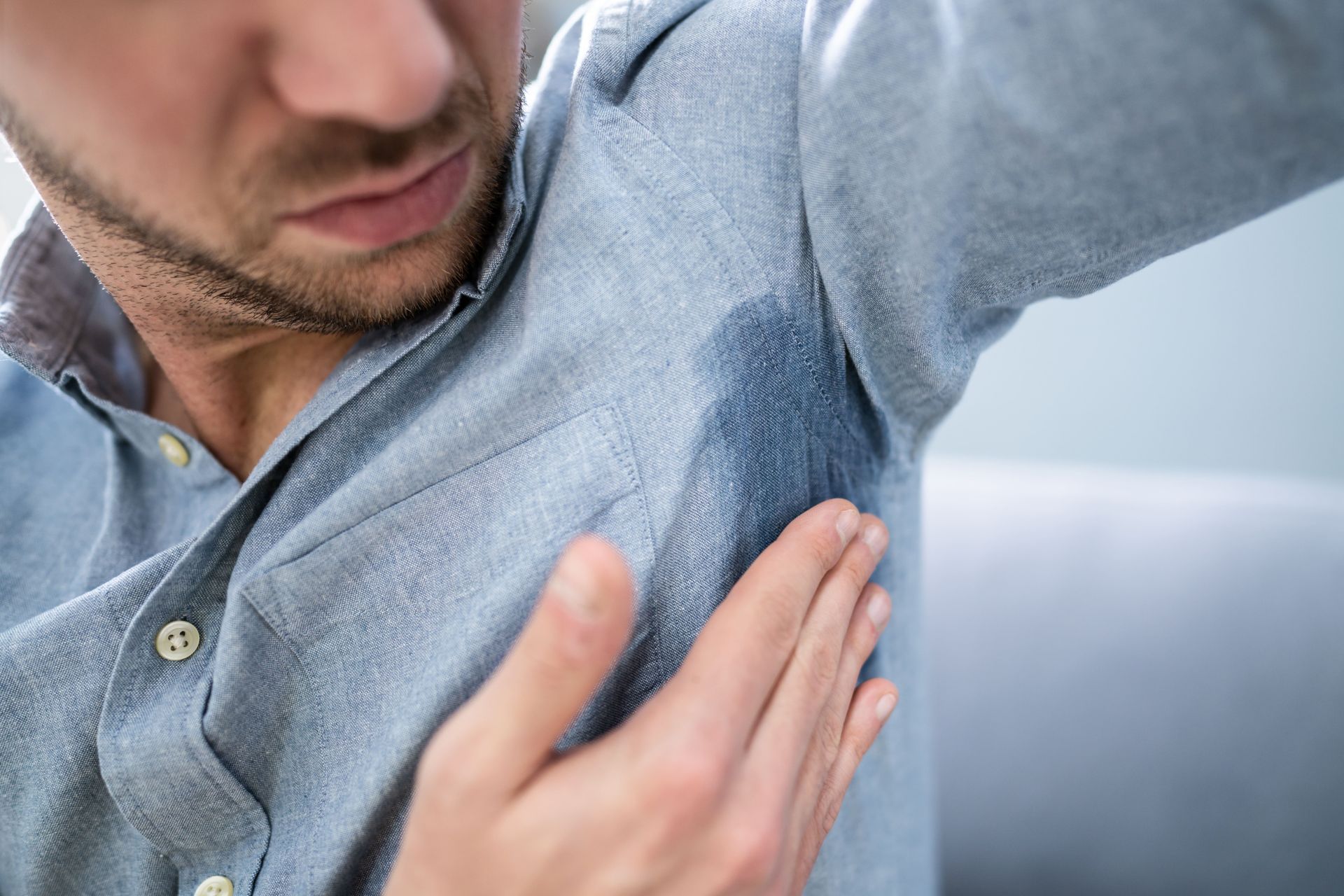 Homem com marca de suor excessivo na camisa, associada a sintomas de hiperidrose
