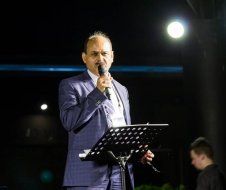 A man in a suit is standing at a podium holding a microphone.