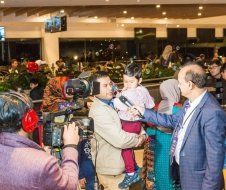 A man is holding a baby while being interviewed by a cameraman.