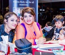 A group of people are sitting at a table with a sign that says henna body art for all occasions.