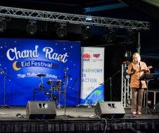 A woman is singing into a microphone on a stage at the chand raat eid festival.