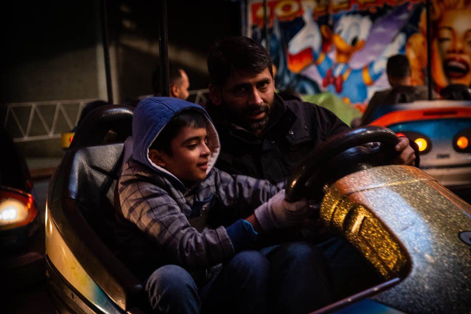 A man and a boy are riding a bumper car at an amusement park.