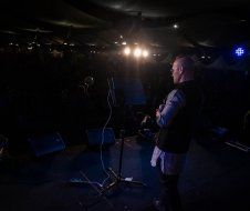 A man is standing on a stage in the dark holding a microphone.
