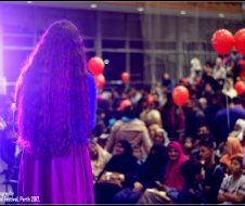 A woman in a purple dress is standing in front of a crowd of people.