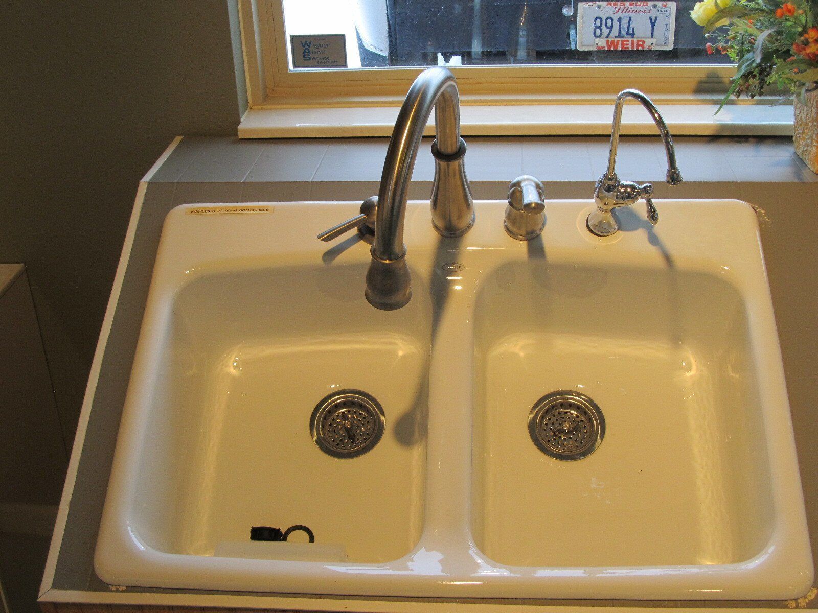 Double kitchen sink with a tall faucet beside a window, white basin and chrome fixtures
