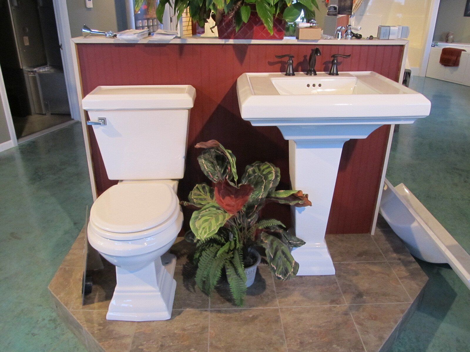 White toilet and pedestal sink with a potted plant between them in a small restroom display.