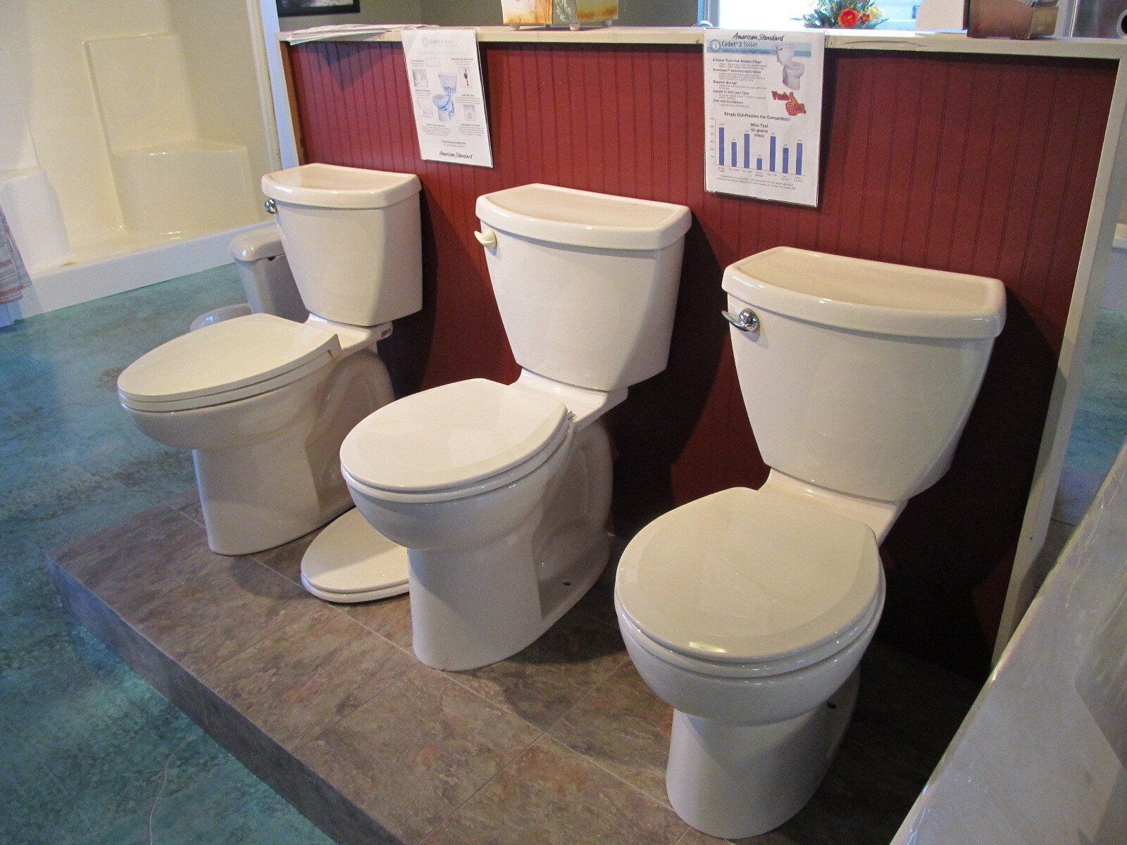 Public restroom with three white toilets lined up against a red wall.