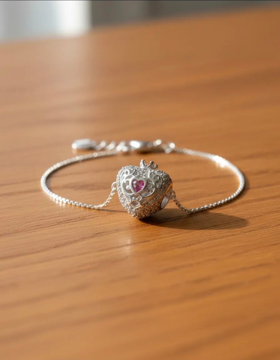 Pulsera de plata con un dije en forma de corazón sobre una mesa de madera.
