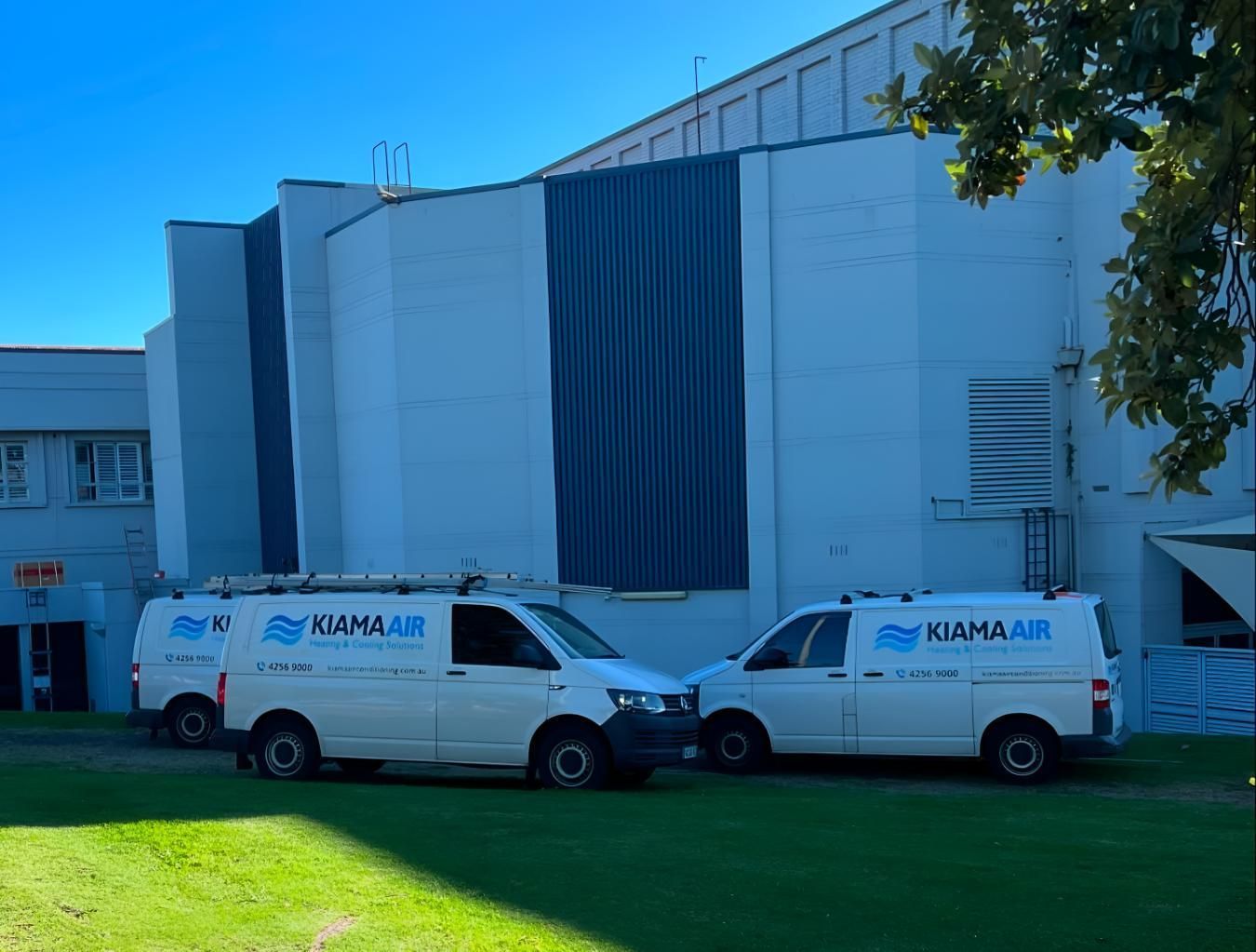 Two White Vans Are Parked in Front of a Large White Building — Kiama Air Conditioning in Albion Park Rail, NSW