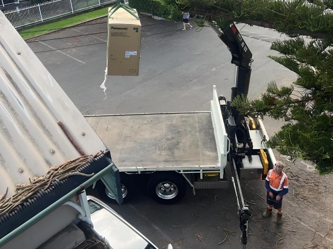 Man is Standing Next to a Truck That is Lifting a Box — Kiama Air Conditioning in Albion Park Rail, NSW
