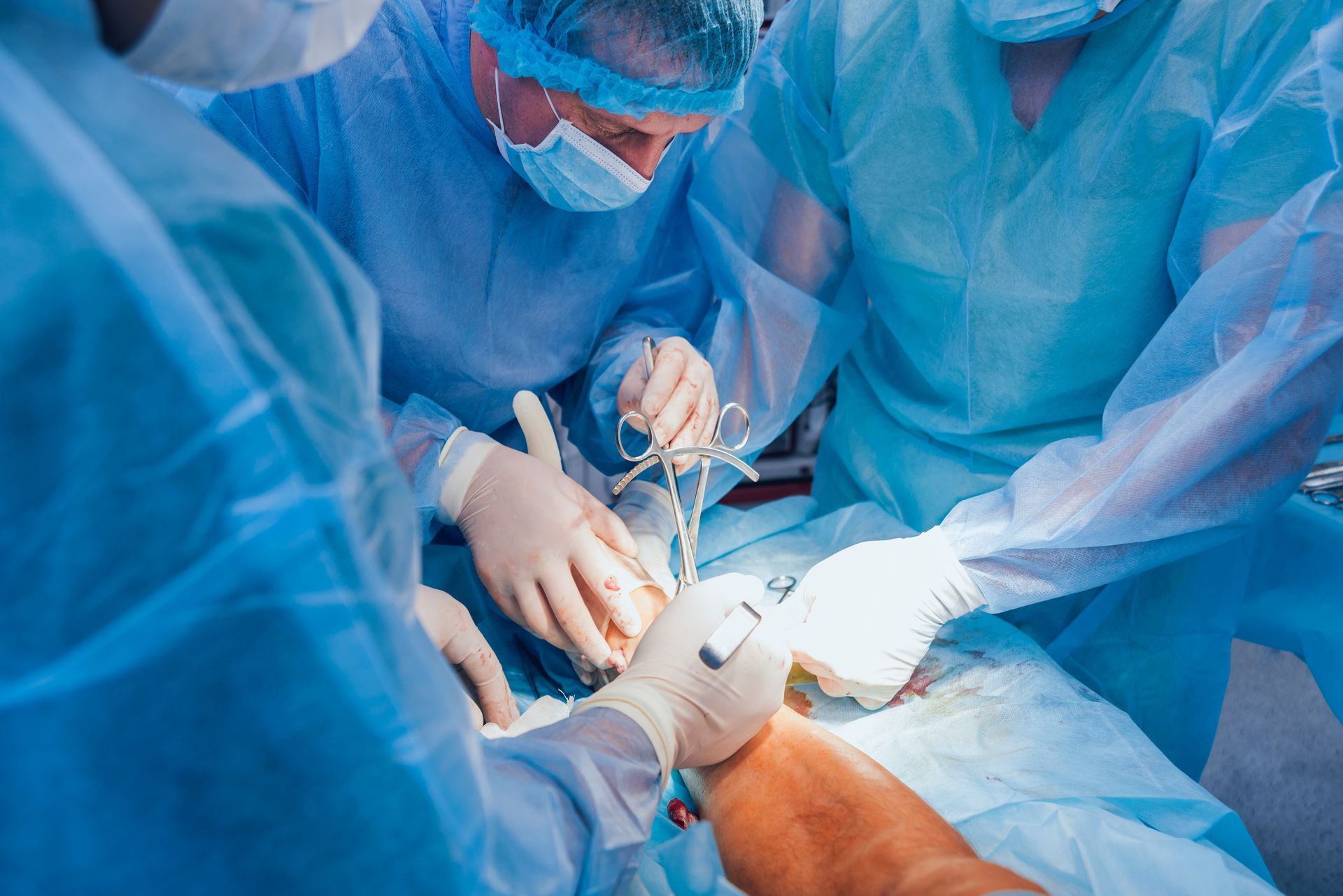 Surgeons in blue scrubs perform surgery on a patient, illuminated by bright lights.