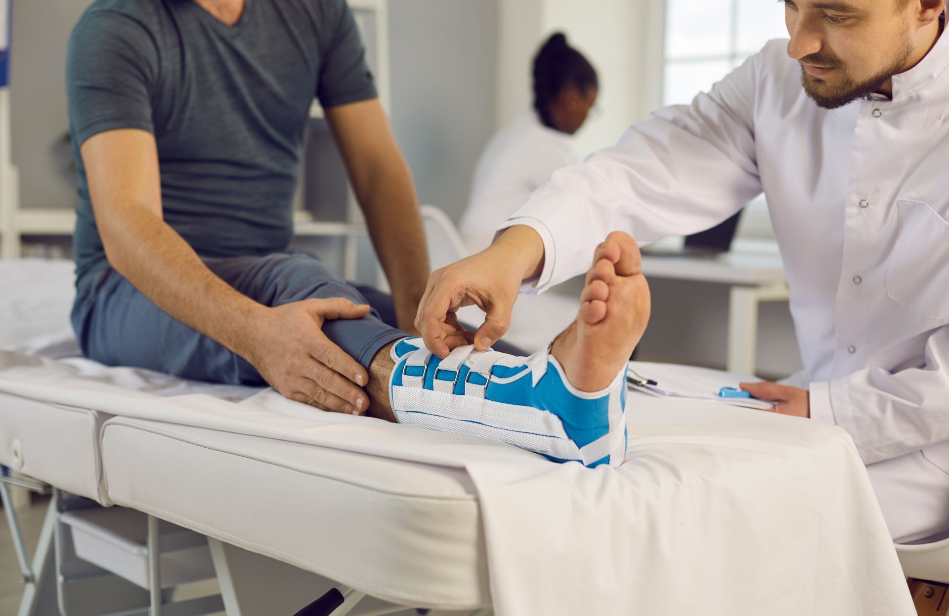 A doctor examining a patient's foot with a blue ankle brace in a medical setting.