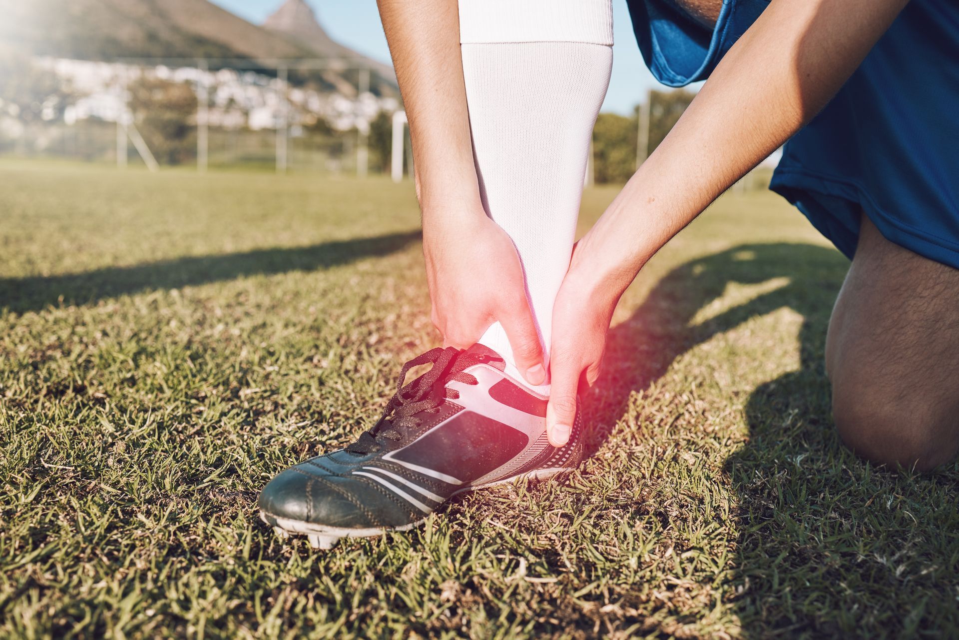 Soccer player clutching ankle on field, red highlight indicating pain.