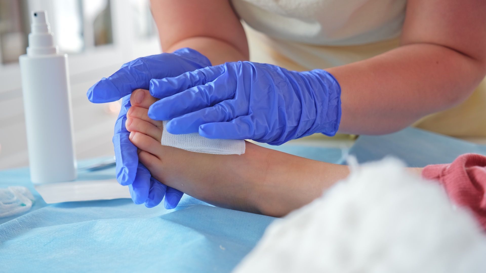 Hands in blue gloves holding a foot, applying a white pad, indoors.