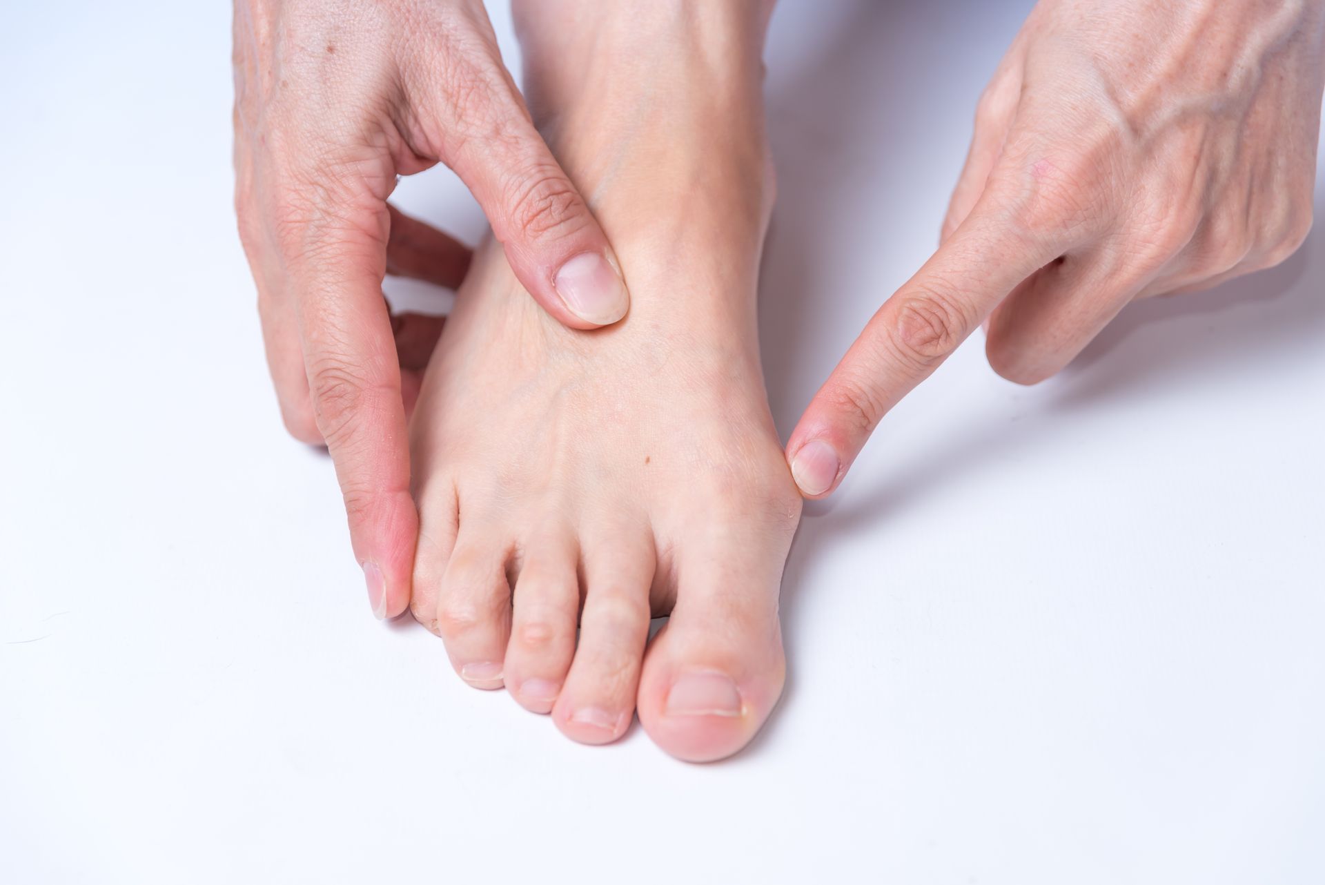 Hand pointing at a foot, possibly examining it. Light skin tone on white background.