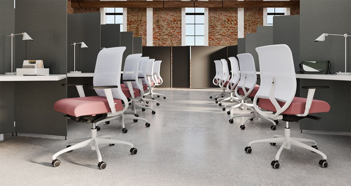 Cubicoli per ufficio con sedie bianche e rosa, pareti grigie, sfondo in mattoni, scrivanie e lampade da scrivania.