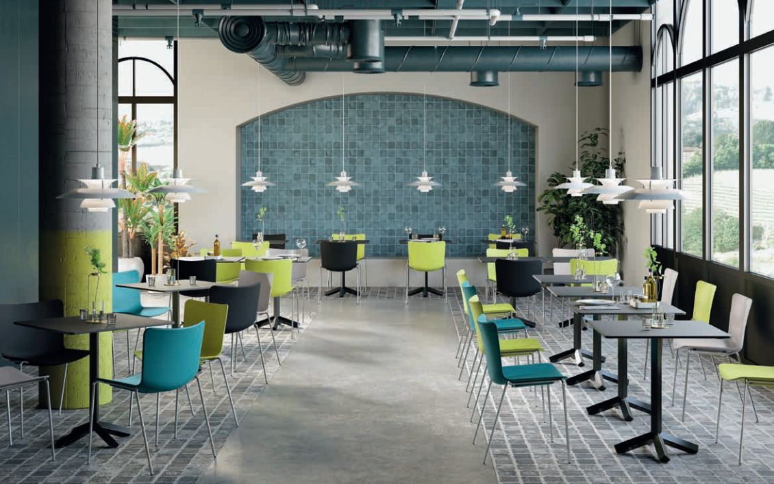 Interno di un bar moderno con sedie colorate, pareti piastrellate e grandi finestre.