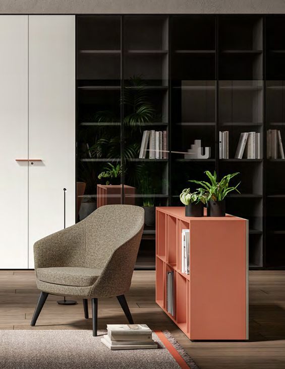 Soggiorno moderno con poltrona beige, credenza color corallo e scaffali a muro scuri con libri e piante.