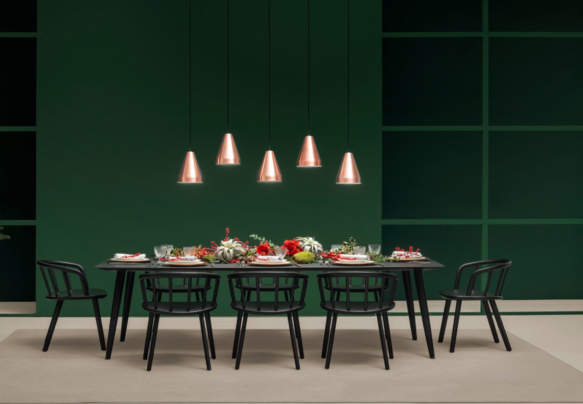 Tavolo da pranzo moderno apparecchiato per una cena in una stanza verde scuro con lampade a sospensione