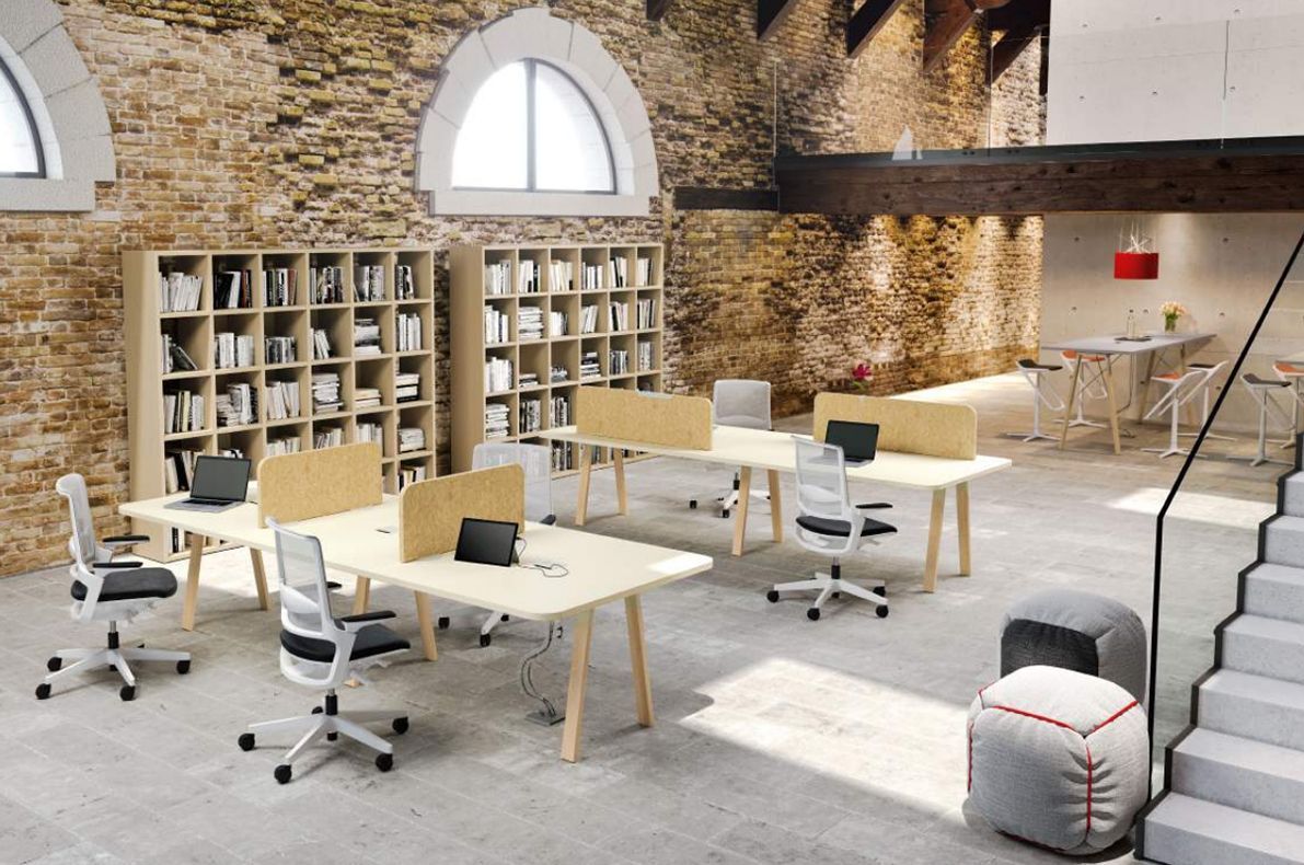 Spazio ufficio con scrivanie, sedie e librerie contro un muro di mattoni.