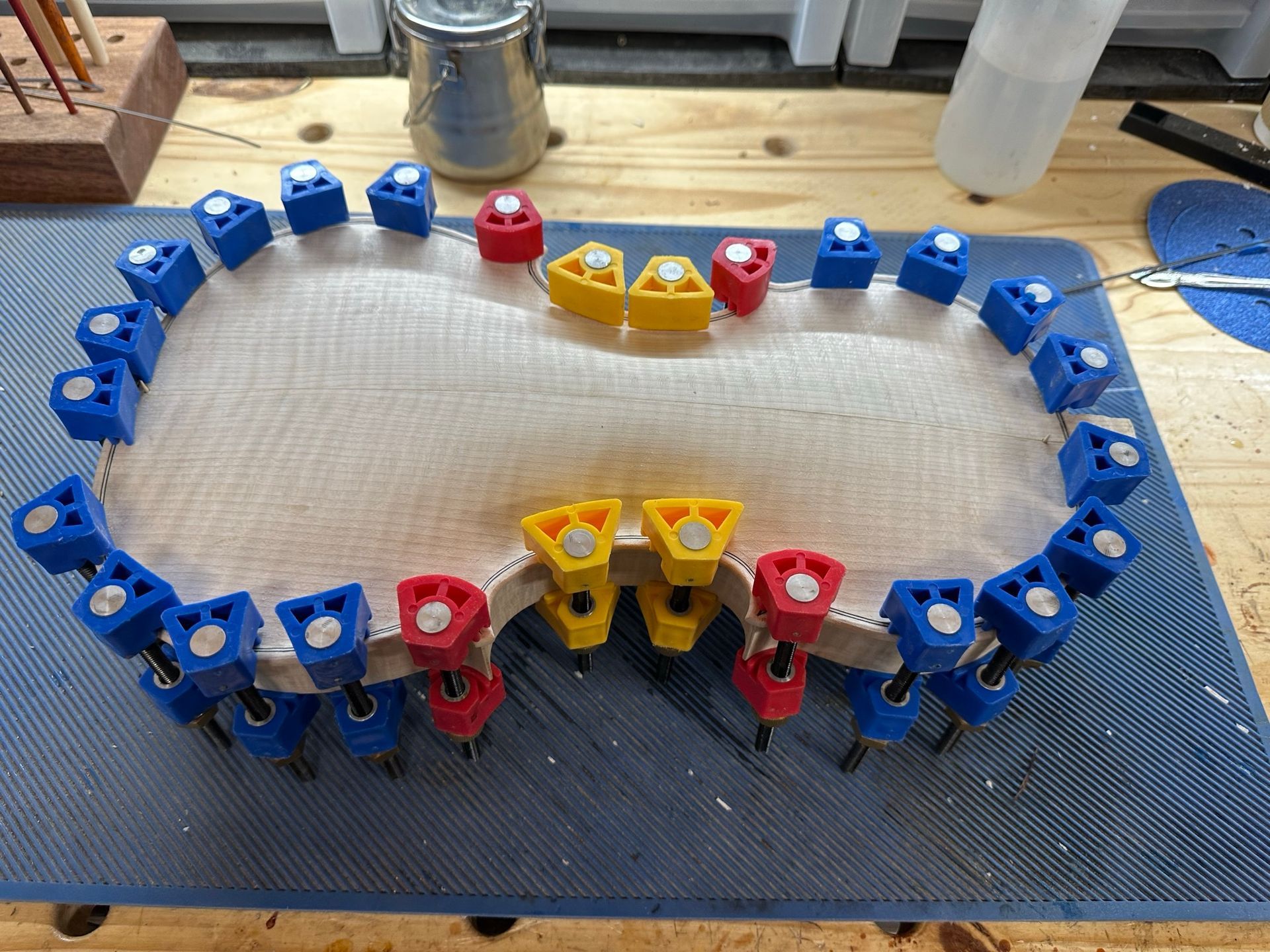 A violin is being glued together with blue and yellow clamps