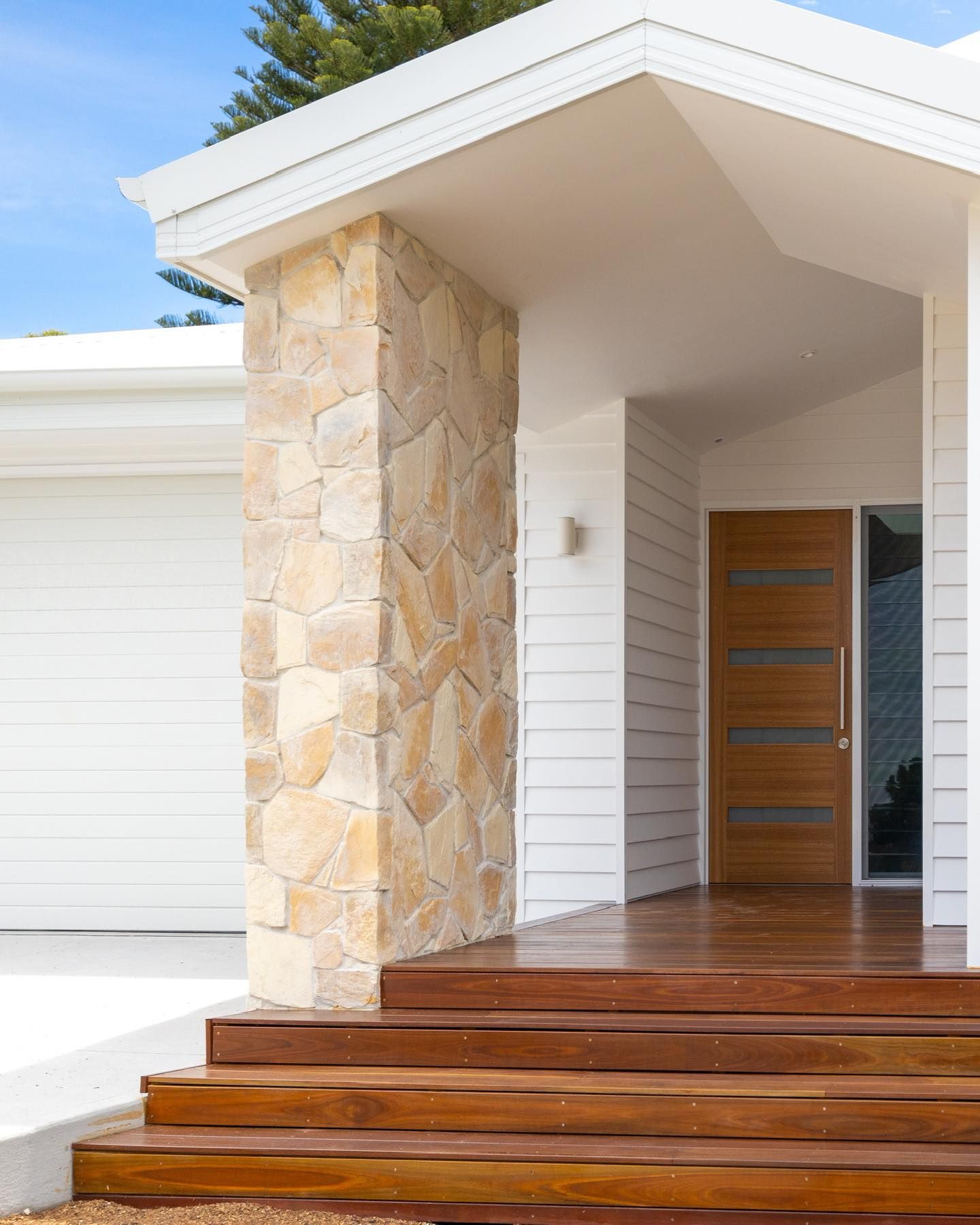 Stone pillar and wooden door on a house porch, with wooden steps leading up. — Blue Horizon Projects in Bateau Bay, NSW