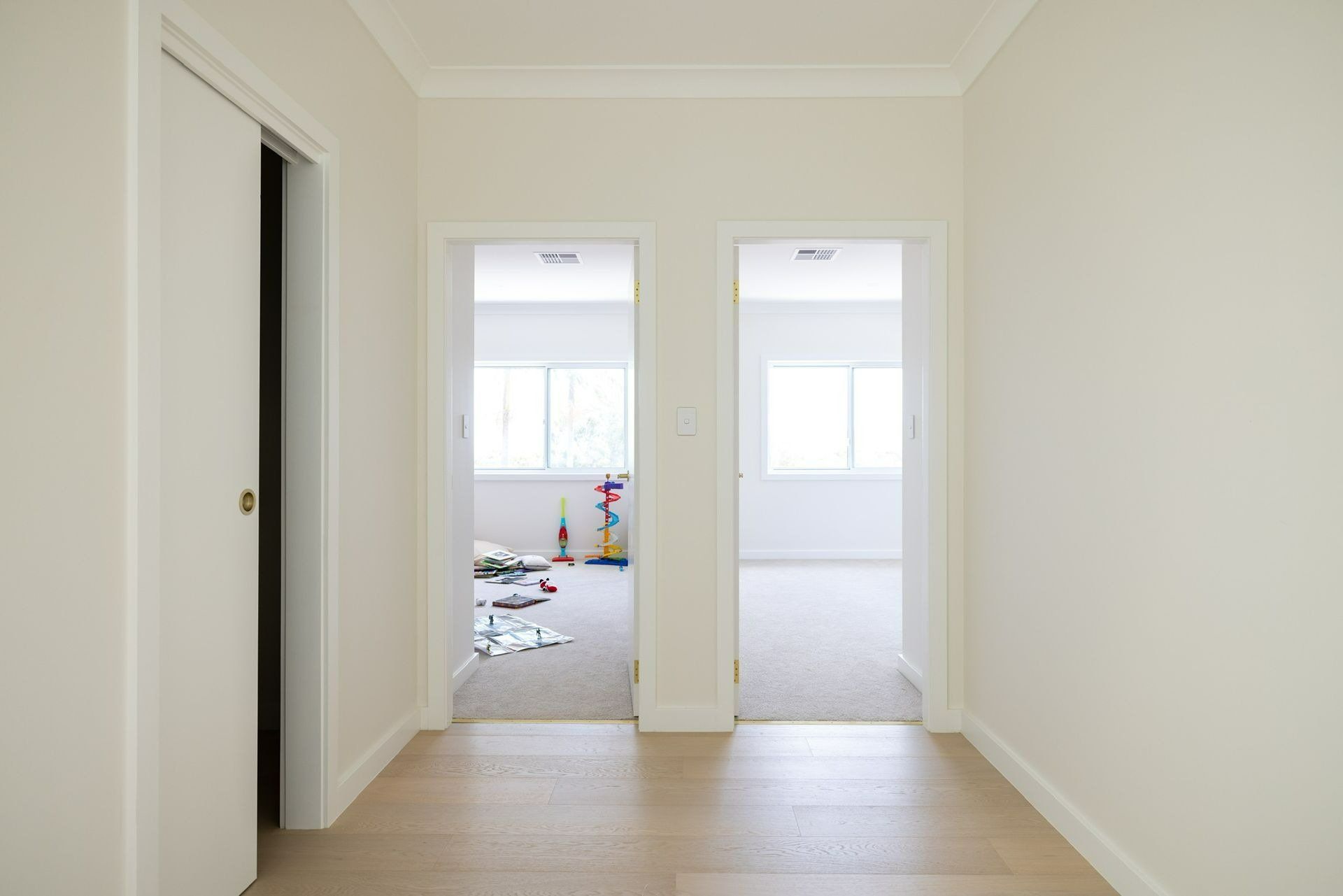 Hallway with two doorways and a closet door. One room messy with toys, the other empty, both with windows. — Blue Horizon Projects in Hunter Valley, NSW