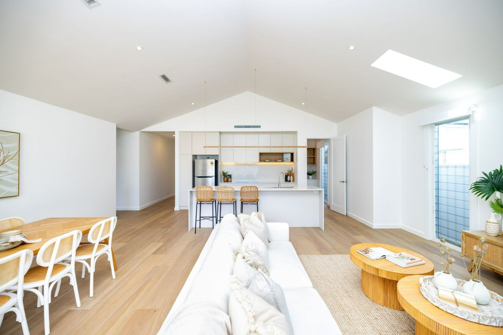 Bright, modern living space with white walls, wood floors, kitchen, dining area, and seating. — Blue Horizon Projects in Bateau Bay, NSW