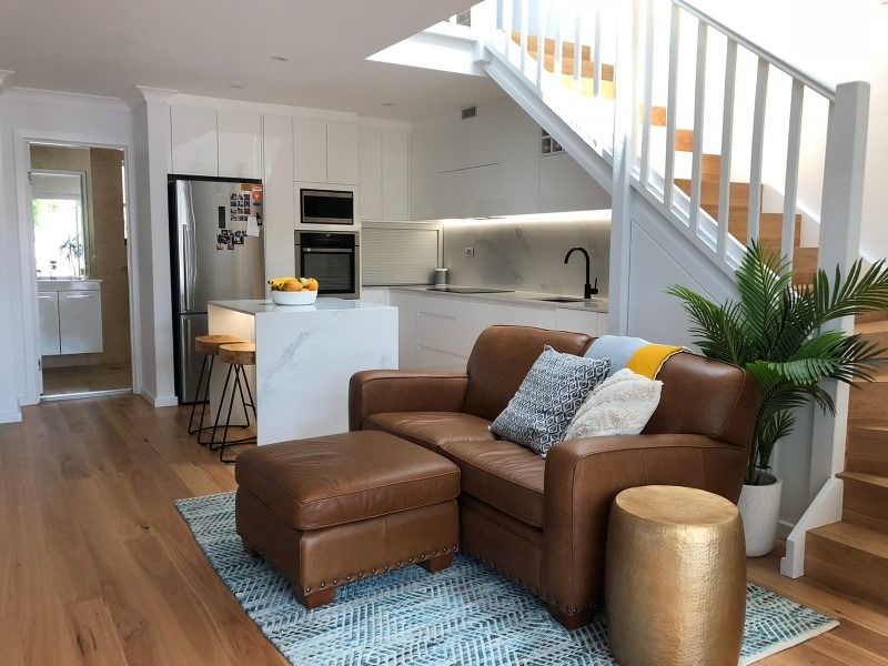A Living Room with A Couch, Chair, Ottoman and Stairs Leading to The Kitchen — Blue Horizon Projects in Killarney Vale, NSW