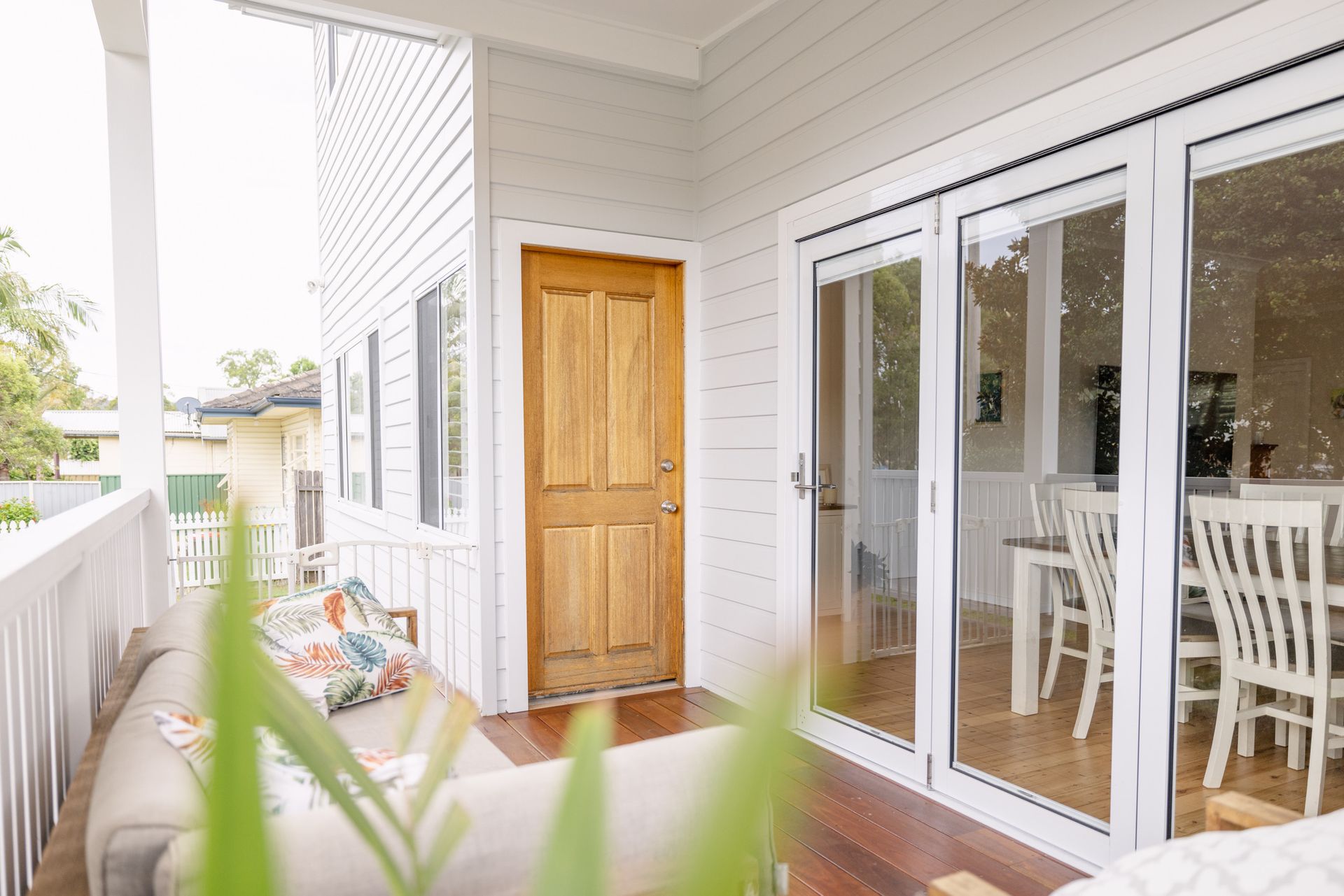 A white porch with a wooden door and glass doors leading to a dining room. — Blue Horizon Projects in Bateau Bay, NSW