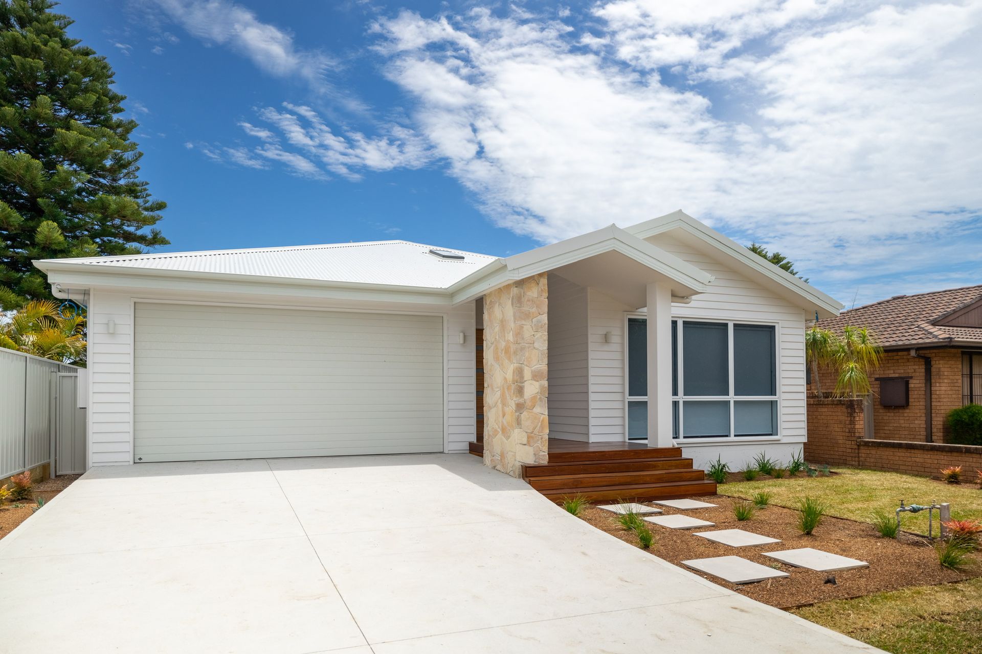 White house with garage, stone accents, and a concrete driveway under a blue sky. — Blue Horizon Projects in Bateau Bay, NSW