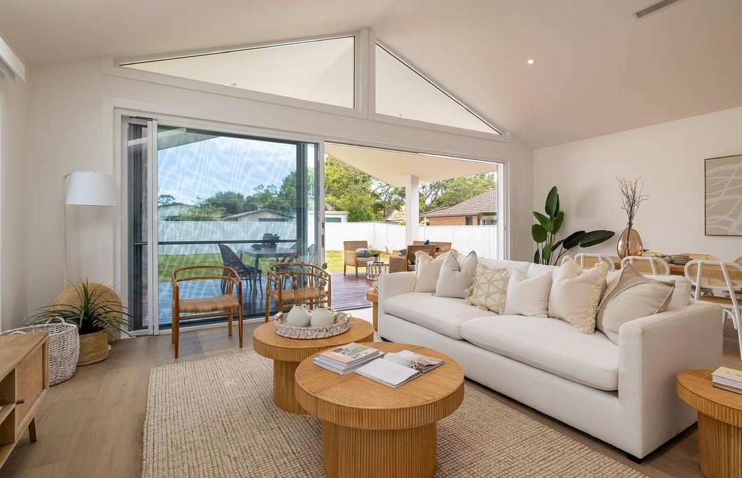 Bright living room with white sofa, open to a backyard. Two wooden coffee tables, rug, and plants. — Blue Horizon Projects in Bateau Bay, NSW