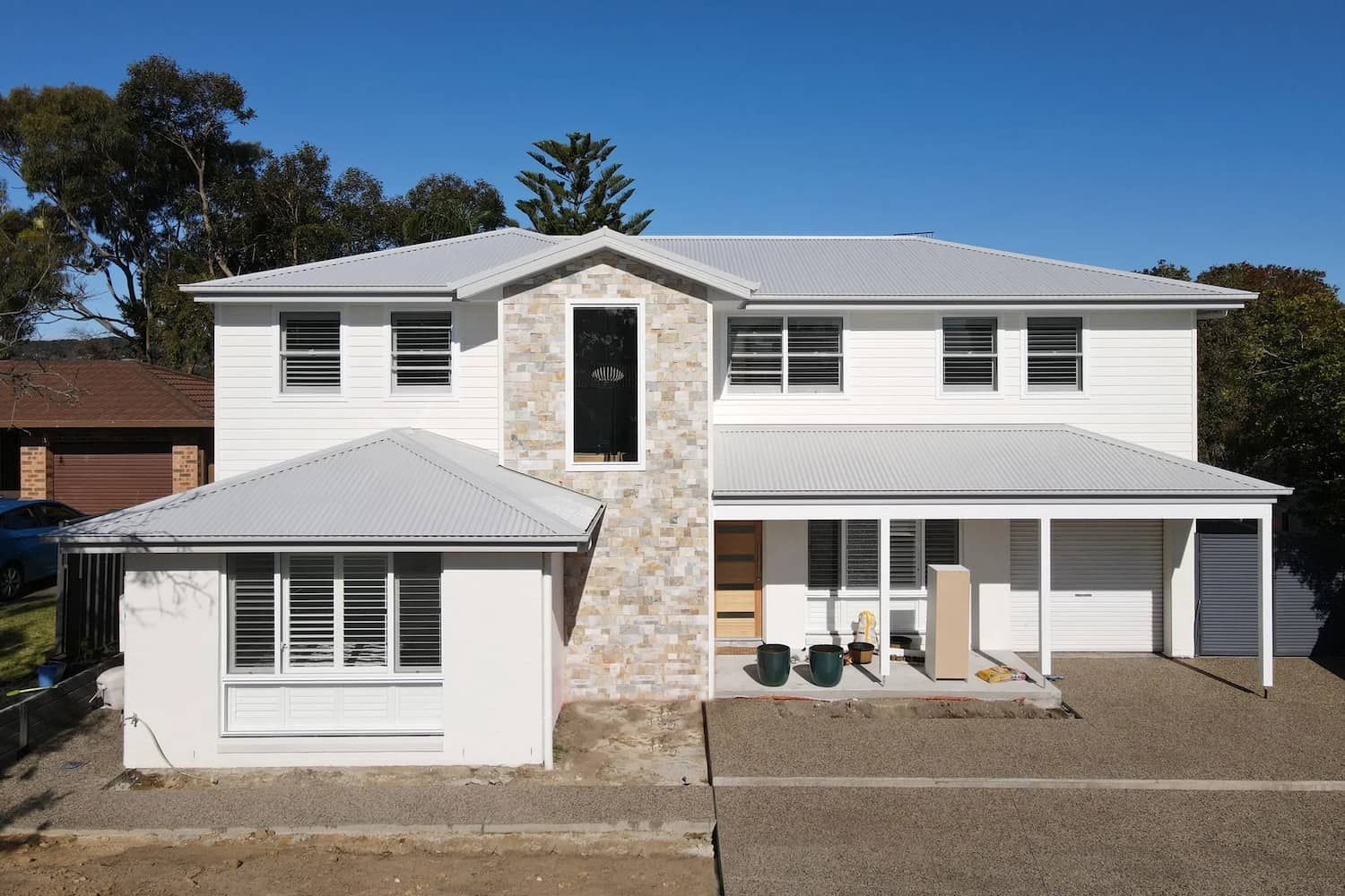 Two-story white house with gray roof, stone accent, and carport on a gravel lot. — Blue Horizon Projects in Bateau Bay, NSW