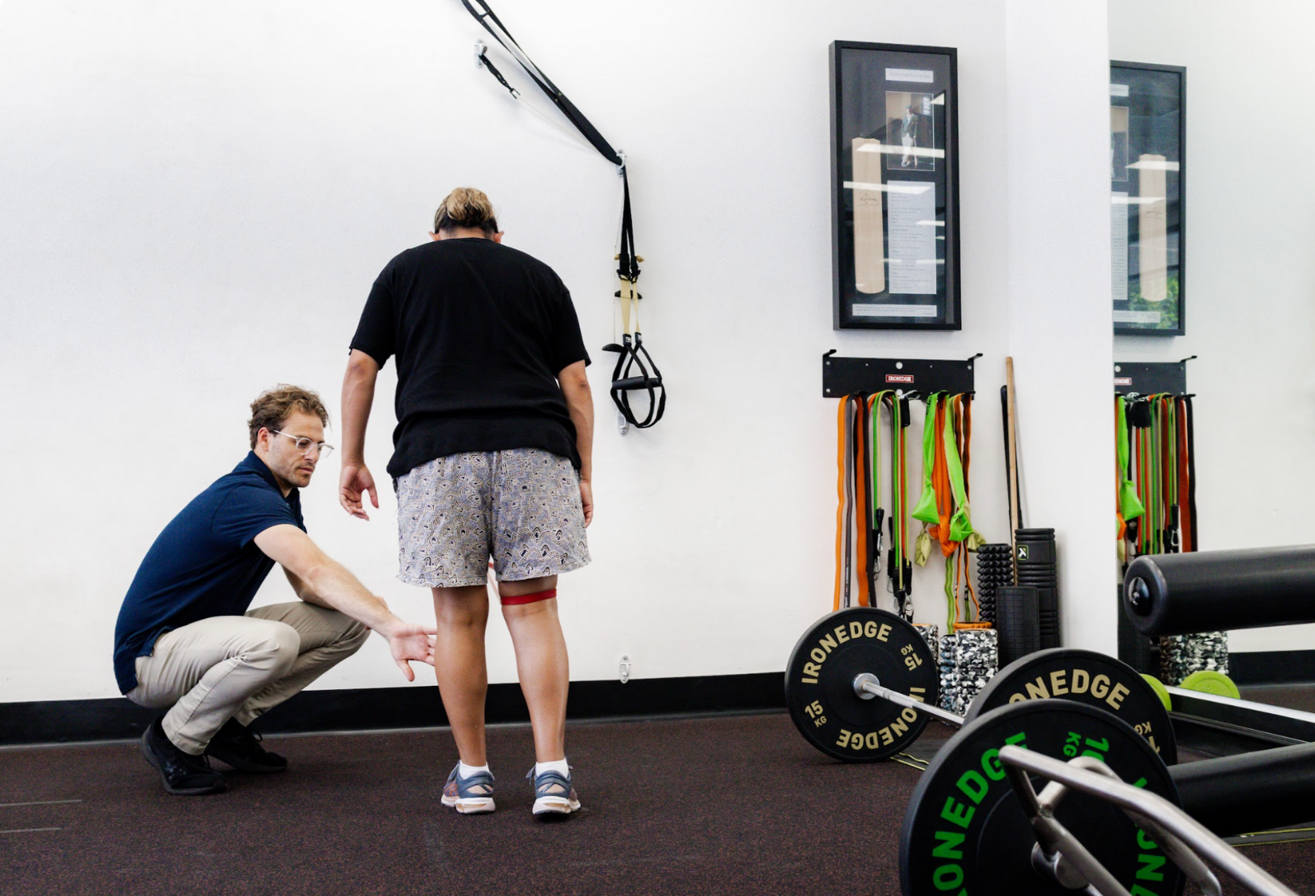 A therapist assisting a person with a resistance band around their legs in a gym setting.