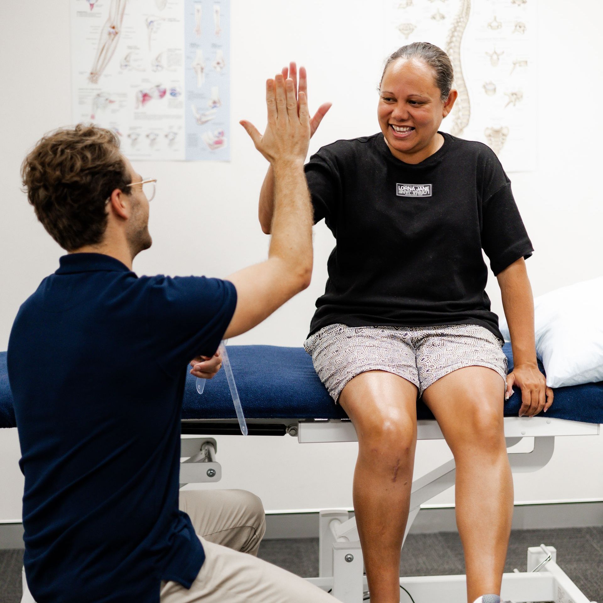Man and woman high-fiving. They are in a medical exam room. The woman is seated on a bed.
