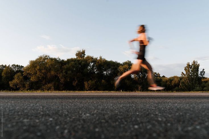 Blurred runner on an asphalt road; trees in the background, blue sky overhead.