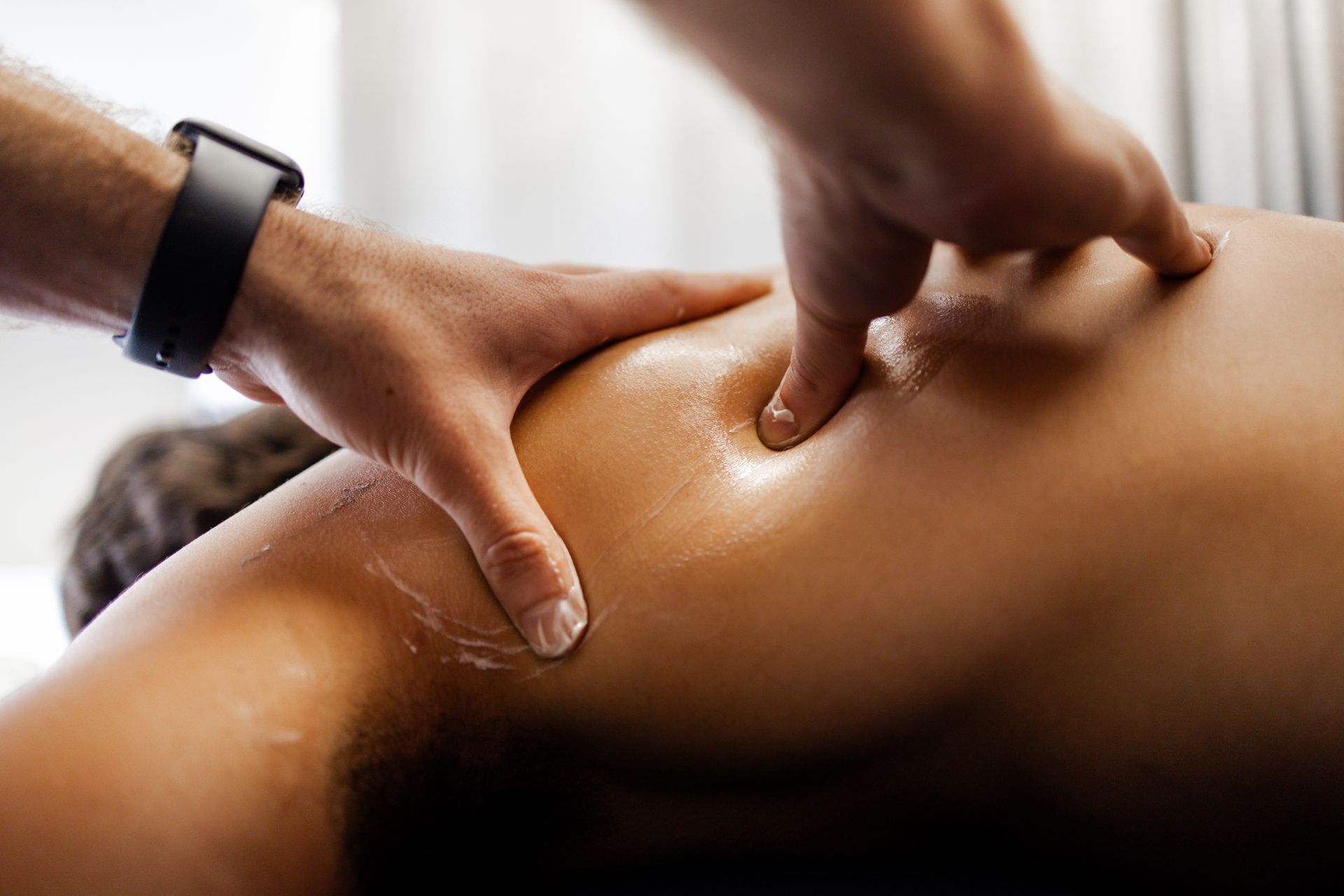 Hands massaging a person's shoulder and back. Oils are visible.