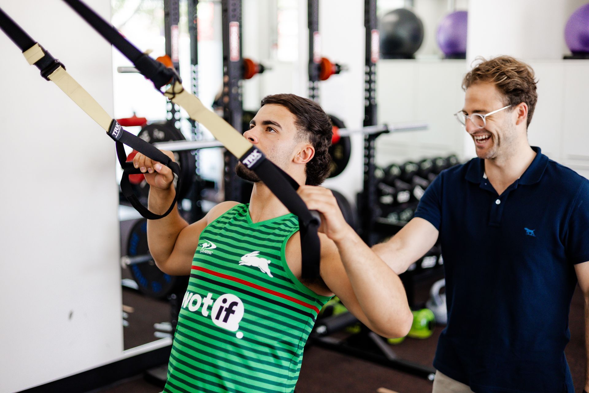 Man using TRX suspension straps, guided by an instructor in a gym setting.