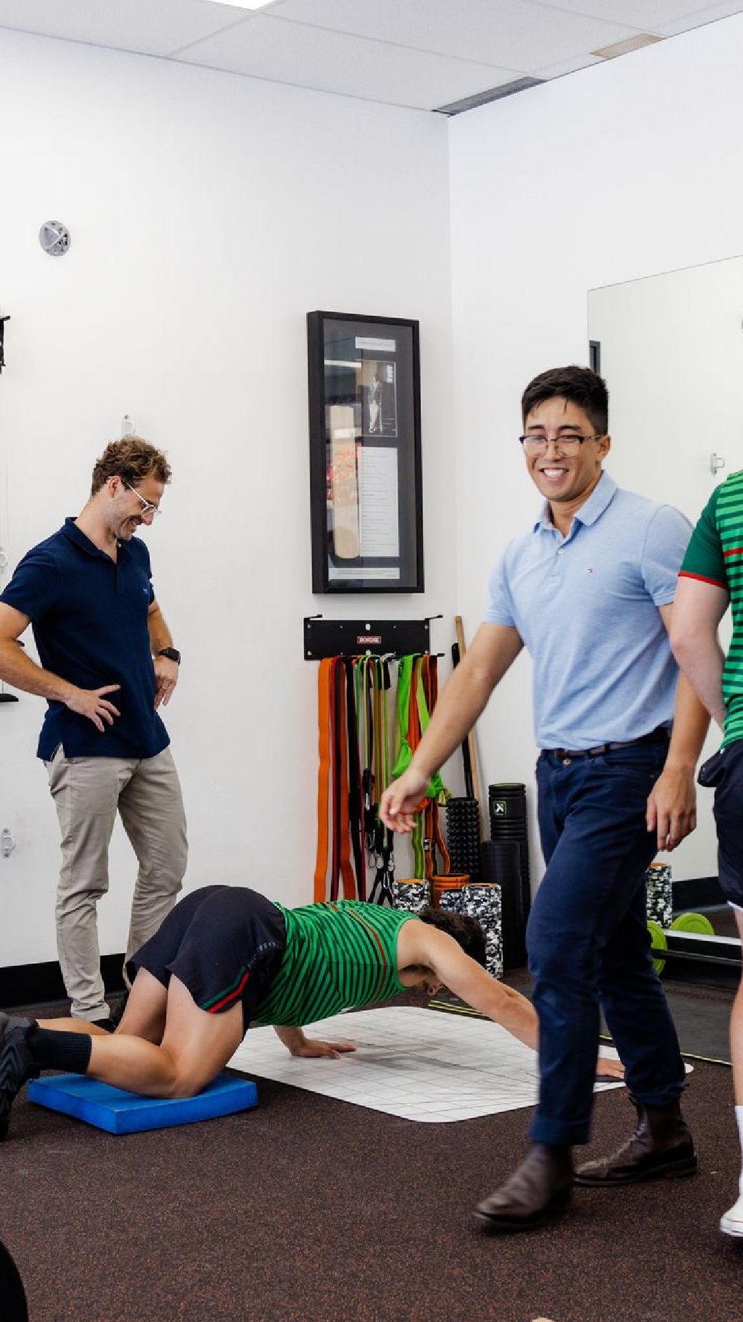 Physiotherapist guides a person doing exercise on floor, two others observe.
