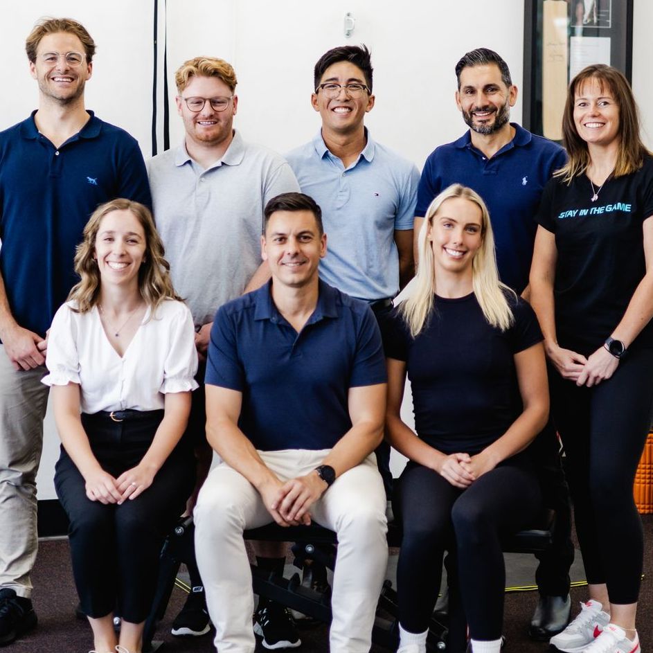 Group photo: Nine people smiling at the camera. They are in a clinic, wearing casual attire.