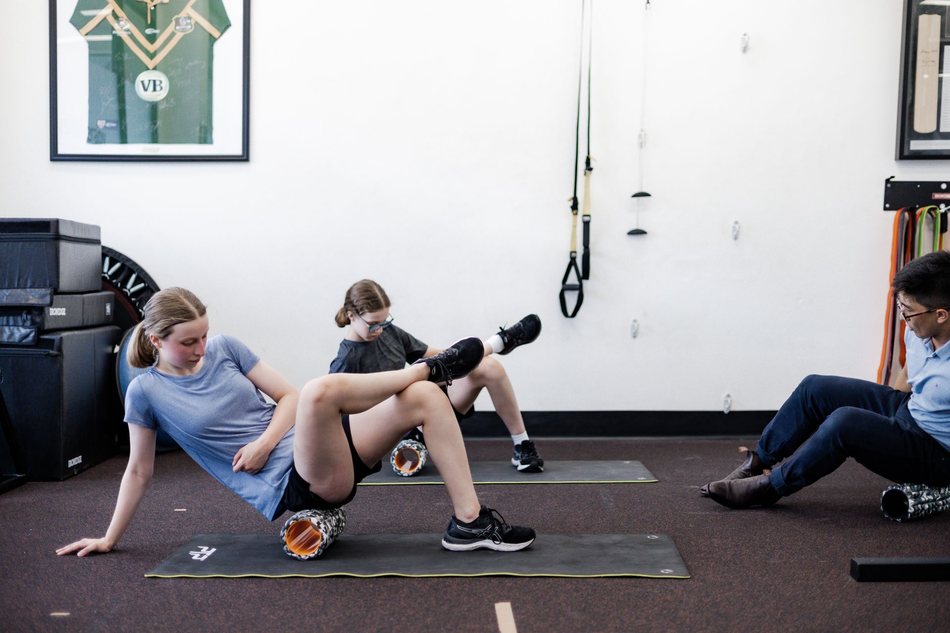 People rolling out muscles with foam rollers on mats in a gym.