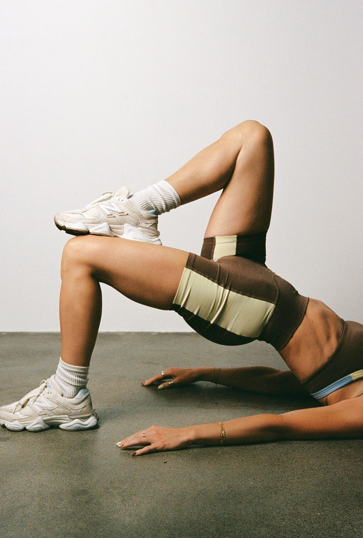 Person doing a bridge pose on a mat in a gym, wearing white sneakers and green shorts.