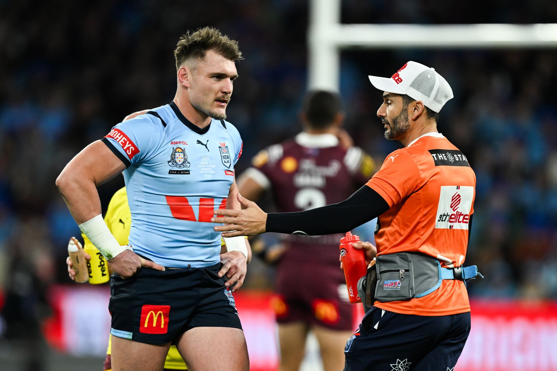 Rugby player in blue jersey talking with medical staff on the field.
