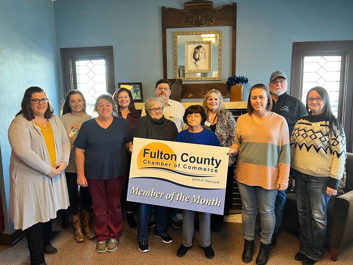 A group of people holding a "Fulton County Chamber & Tourism" sign in an indoor setting.