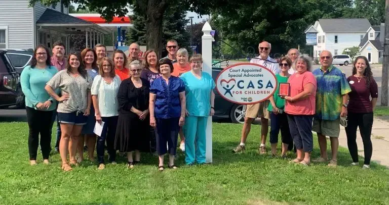 A group of people standing together outdoors on grass next to a sign for 