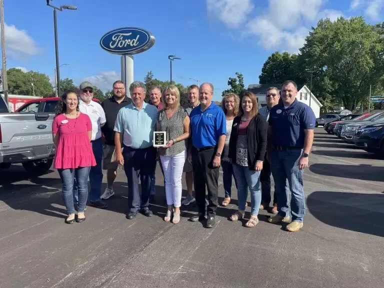 A group of people standing together at a Ford dealership, with one person holding a small award.
