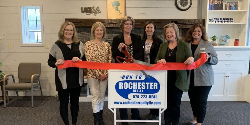 Six people holding red ribbon during a ribbon-cutting ceremony in front of a sign for Rochester Main Street.